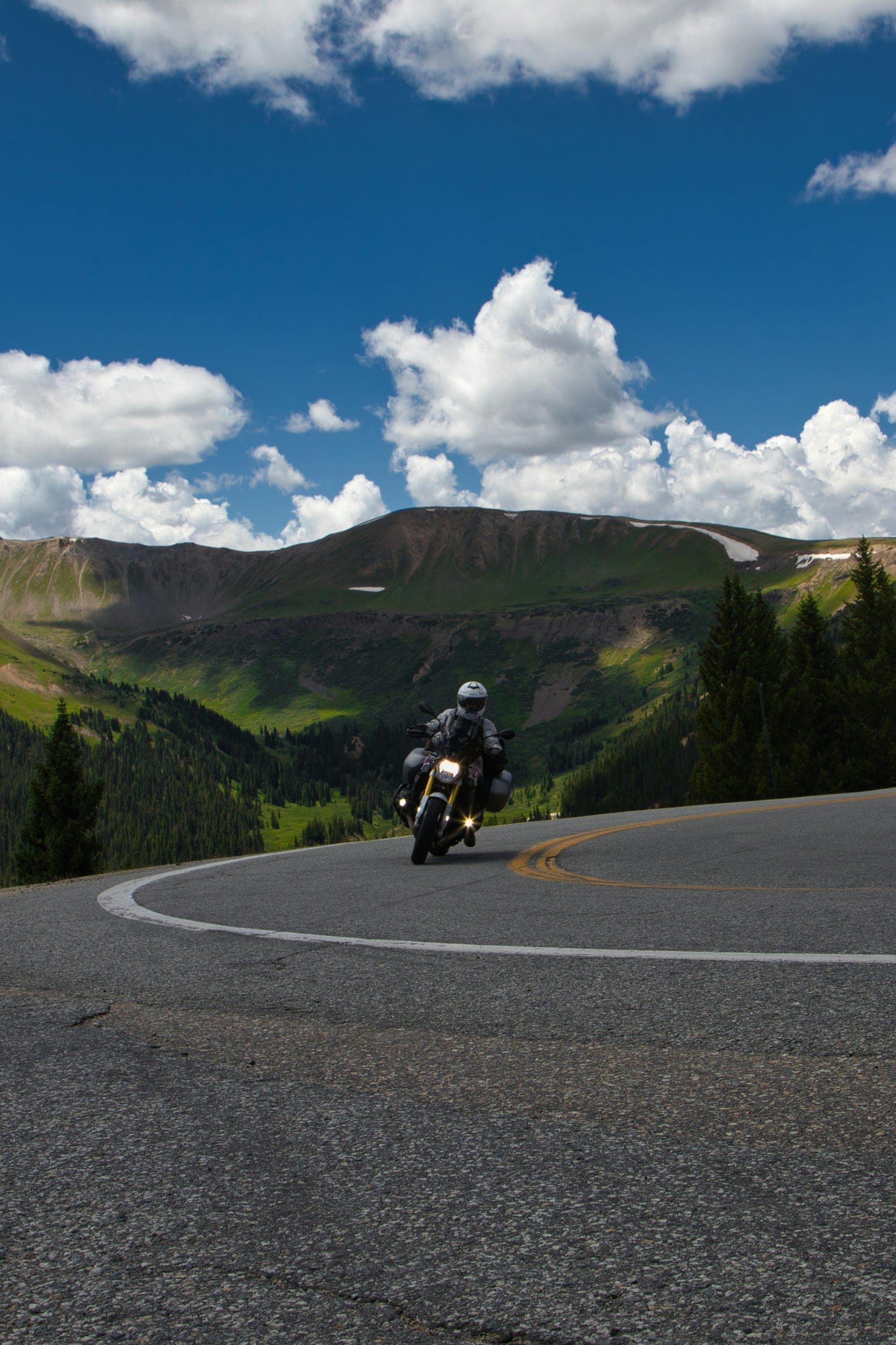 A rider on a loaded touring bike climbing Independence Pass, Colorado, with peaks behind