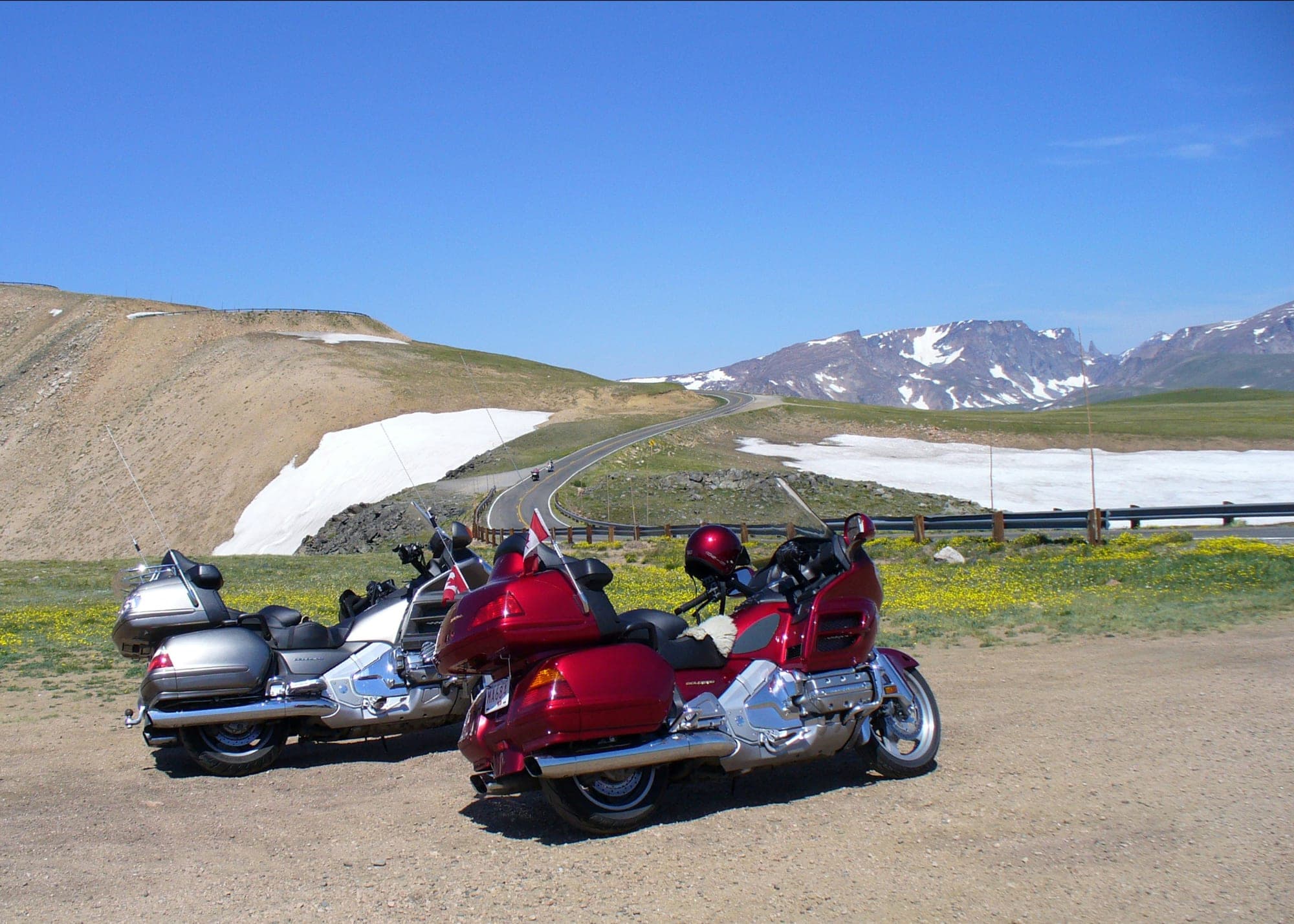 Two touring bikes parked at the top of Beartooth Pass, with snowfields and the highway behind them