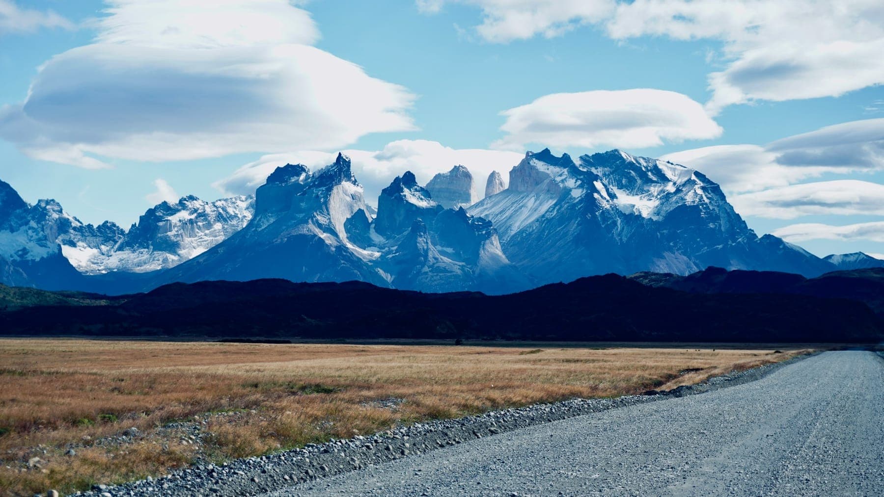 A gravel road heading toward the snow-capped towers of Torres del Paine under lenticular clouds