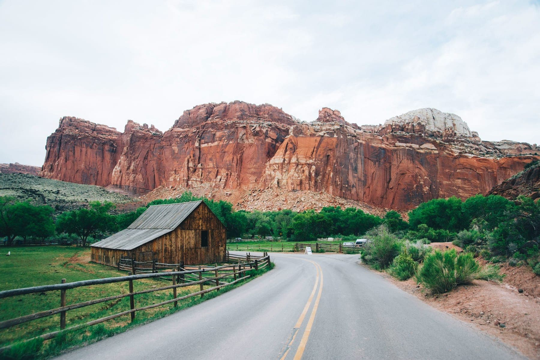 The park road curving past a pioneer barn beneath the red cliffs at Fruita in Capitol Reef